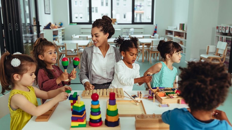 Une assistante maternelle assise à une table avec plusieurs jeunes enfants jouant à des jeux.