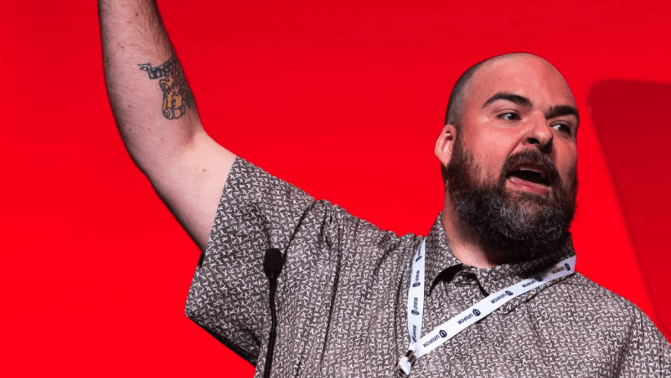 A man speaking at a podium on a red background with his fist raised high 