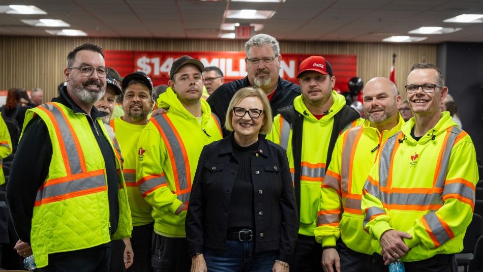 A woman stands in the centre of a group of men in yellow safety shirts