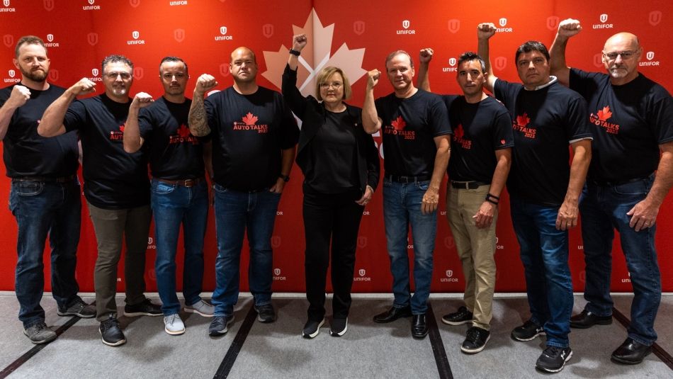 A group of people raise their fists in the air with the Unifor red backdrop behind them.