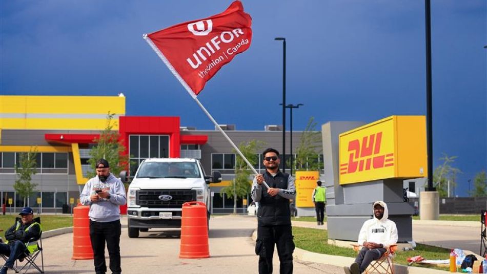 A man holding a large red Unifor flag outside at a DHL facility in Hamilton