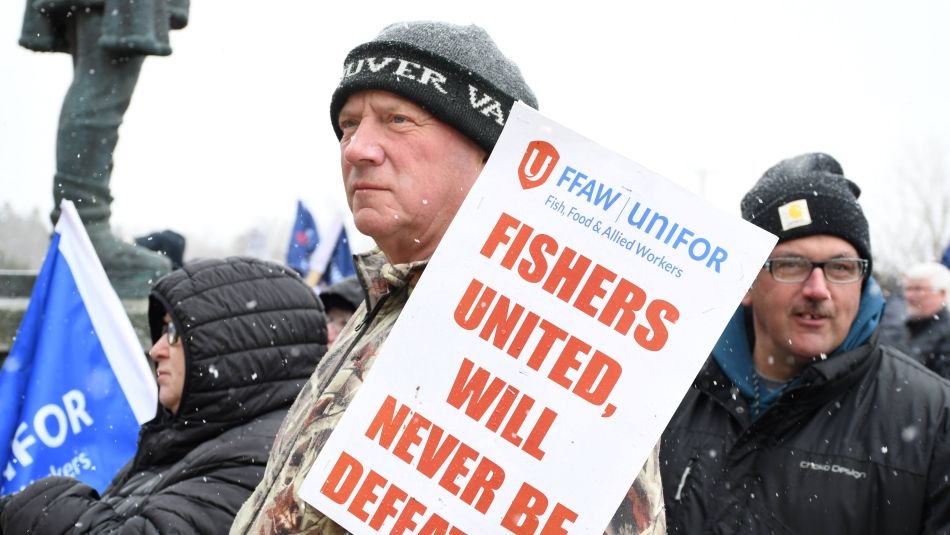 Un membre de SPATA-Unifor tient une pancarte sur laquelle on peut lire "Fishers United Will Never be Defeated" (Les pêcheurs unis ne seront jamais vaincus) lors d'un rassemblement à St. John's, Terre-Neuve et Labrador.