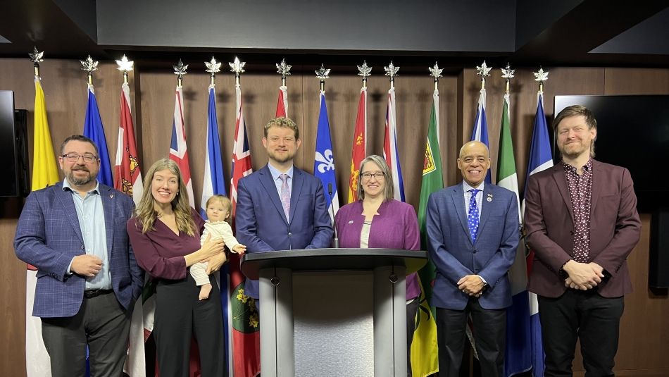 Unifor Quebec Director stands at the left-hand of a group of 7 people, with a backdrop of Canadian provincial flags.