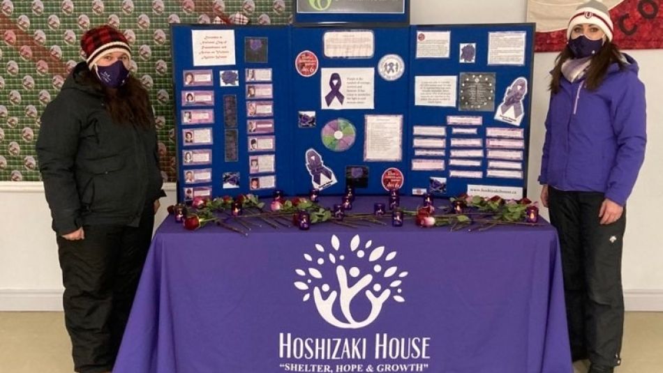 Two women wearing masks standing next to a table, draped in purple.