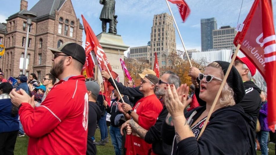 A group of Unifor members clapping and holding flags outside of Queen’s Park in Toronto.