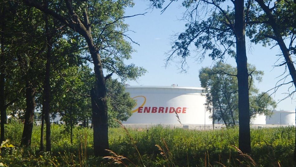 Réservoir de stockage de carburant de la marque Enbridge au loin avec des arbres au premier plan