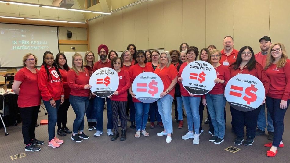 Un groupe de militants d'Unifor, vêtus de chemises rouges identiques et tenant des pancartes sur lesquelles on peut lire "close the gender pay gap" (combler l'écart de rémunération entre les hommes et les femmes)