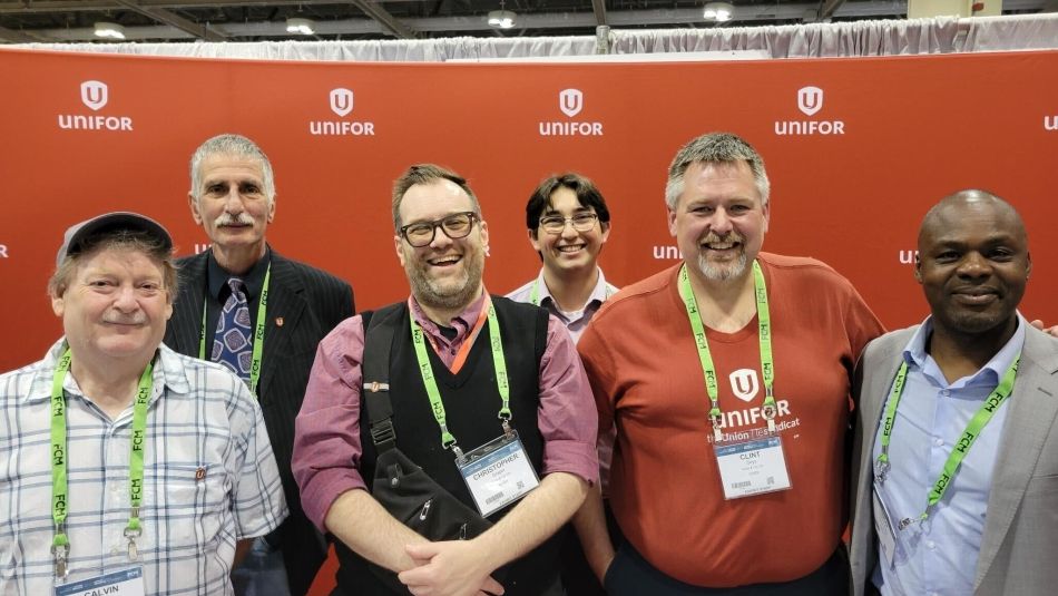 Six people standing in a booth smiling with red Unifor background.
