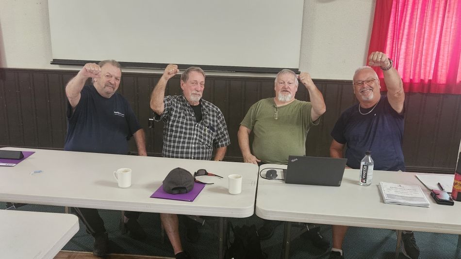 Four people sitting at a table in a row, fists in the air/