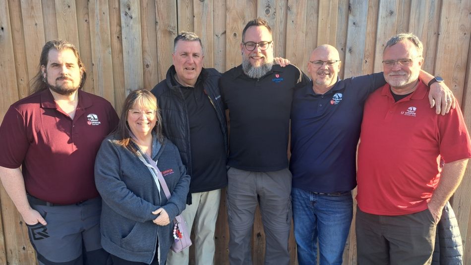 Six people pose outside in fornt of a wooden fence