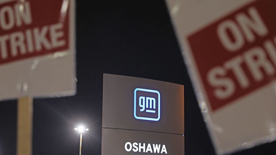 GM picket line in Oshawa On Strike placards with large GM Oshawa signage in the background.