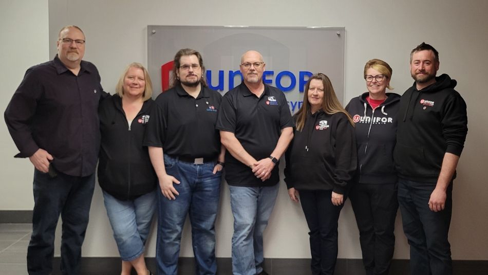 Seven members of Unifor’s Grand River Transit bargaining committee pose together in front of a Unifor sign.
