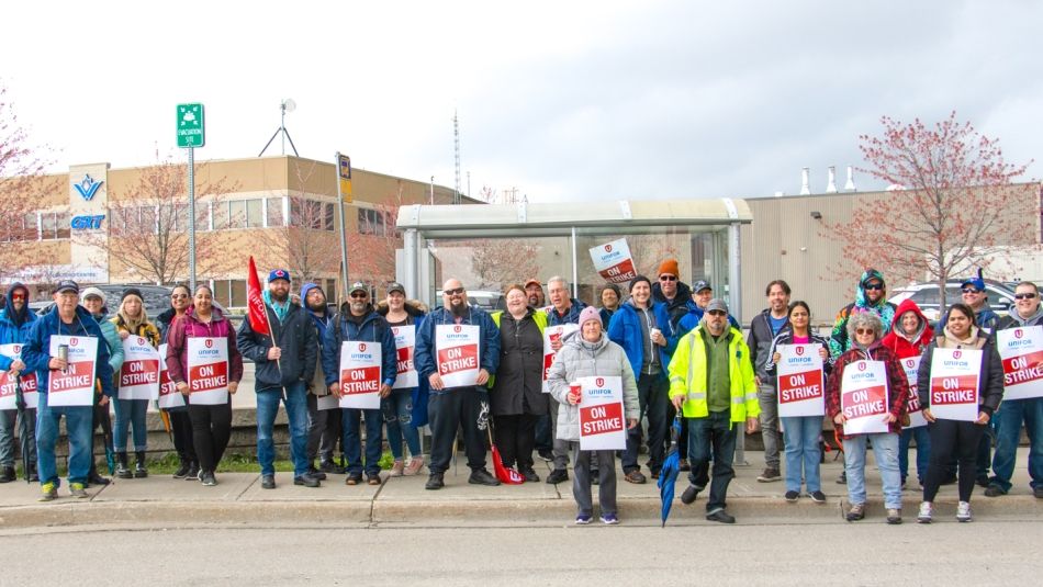 Large group of workers posing for a photo outside, many wearing On Strike placards.