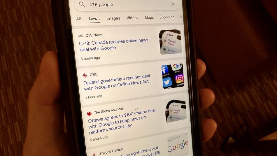 A cell phone being held by a hand, showing Canadian news from Google.