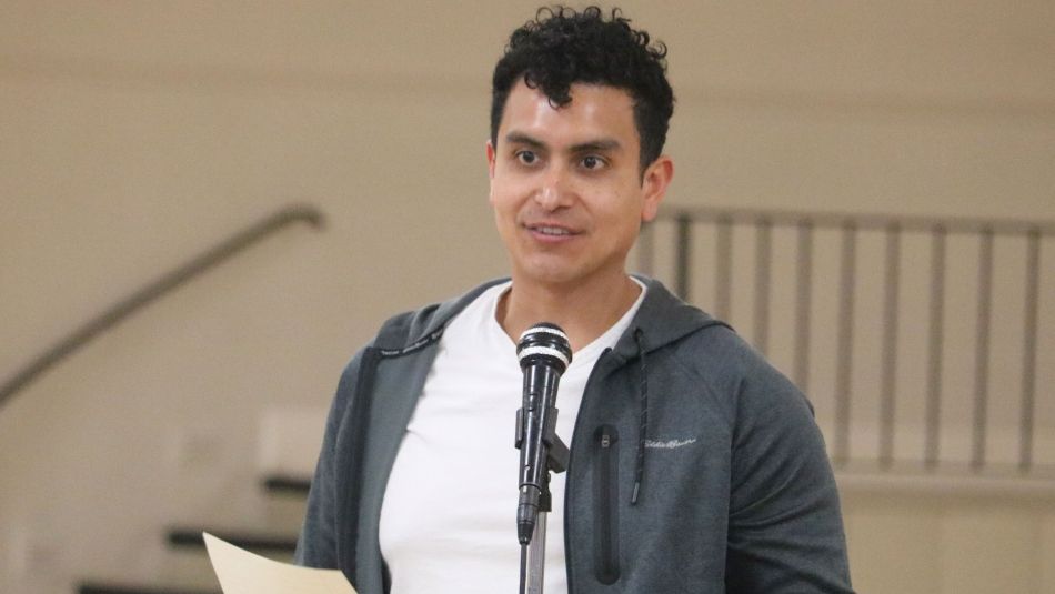 A man speaks at a mic holding papers