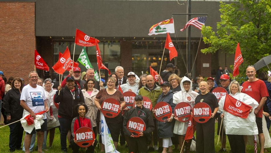 A large group pose outside holding Unifor flags and placcards that read, No two tier American Health Care
