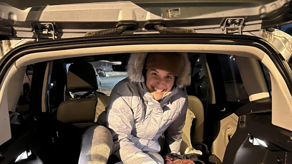 A woman huddles in the back of her vehicle with blankets and coats.