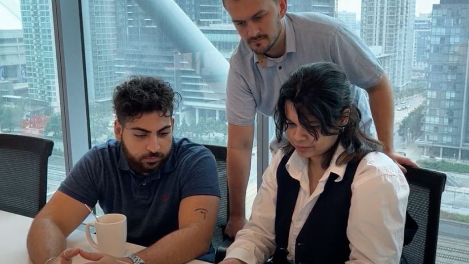 two people sitting at a table looking at papers and a person standing over from behind