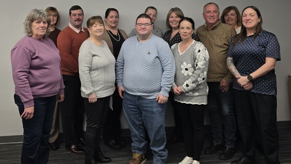 A large group smiling at the camera in front of a beige wall