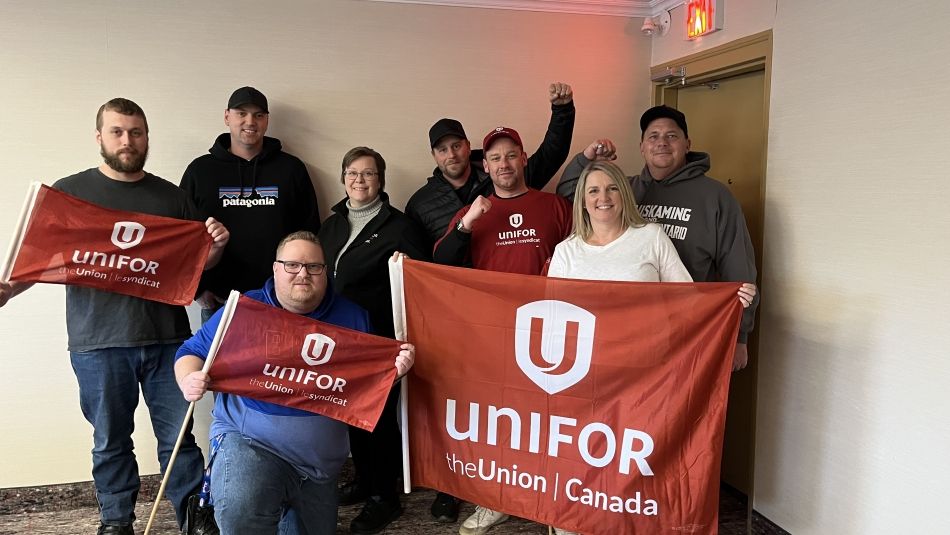 Unifor Local 103 bargaining committee standing together in front of a Unifor flag.