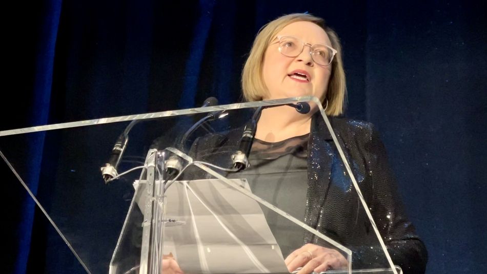 Lana Payne stands at a glass podium, looking to the right of the picture.