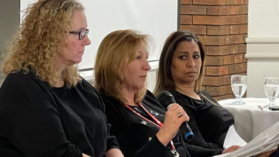 Three women sitting pn a panel, with the middle person speaking into a microphone.