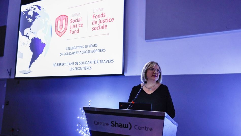 A women speaking at a podium standing in front a presentation screen