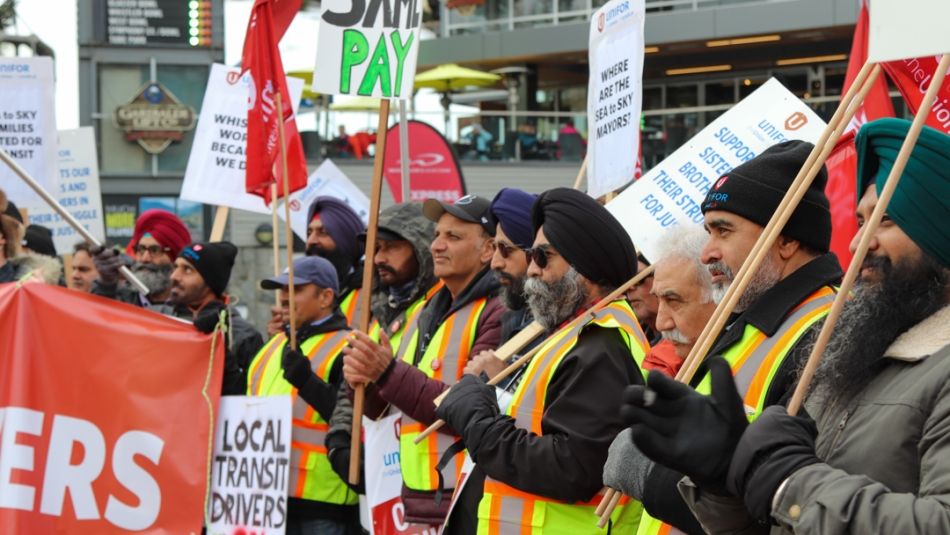 Several transit workers holding flags and placards watching events at a rally.