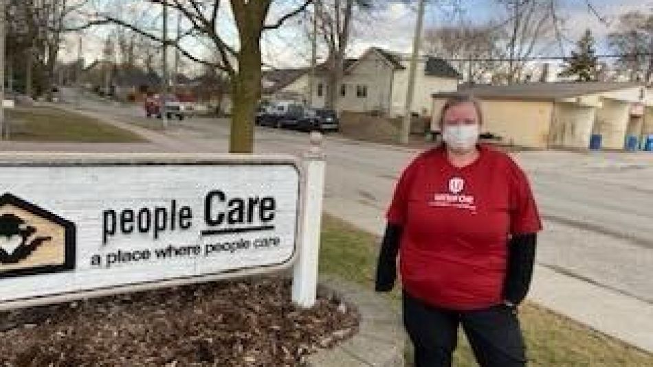 a women in a red Unifor shirt standing beside the peopleCare exertior signage.