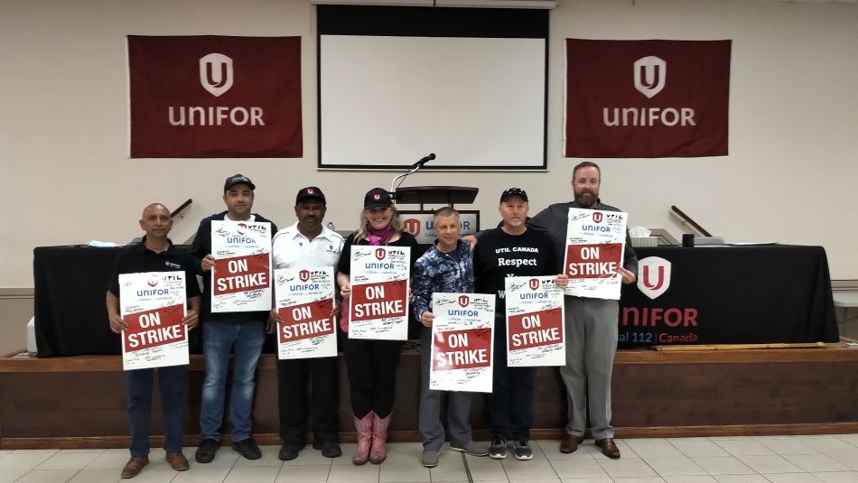 Unifor Local 112 UTIL bargaining committee members and union staff pose with red and white "on strike" placards in hand in front of the main stage at the Local 112 union hall.
