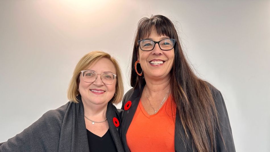 Two women standing together, both wearing poppies on their collars. 