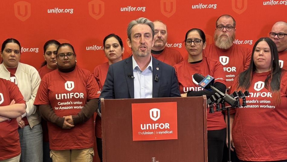 Gavin McGarrigle at a podium in front of Amazon workers and a red unifor backdrop