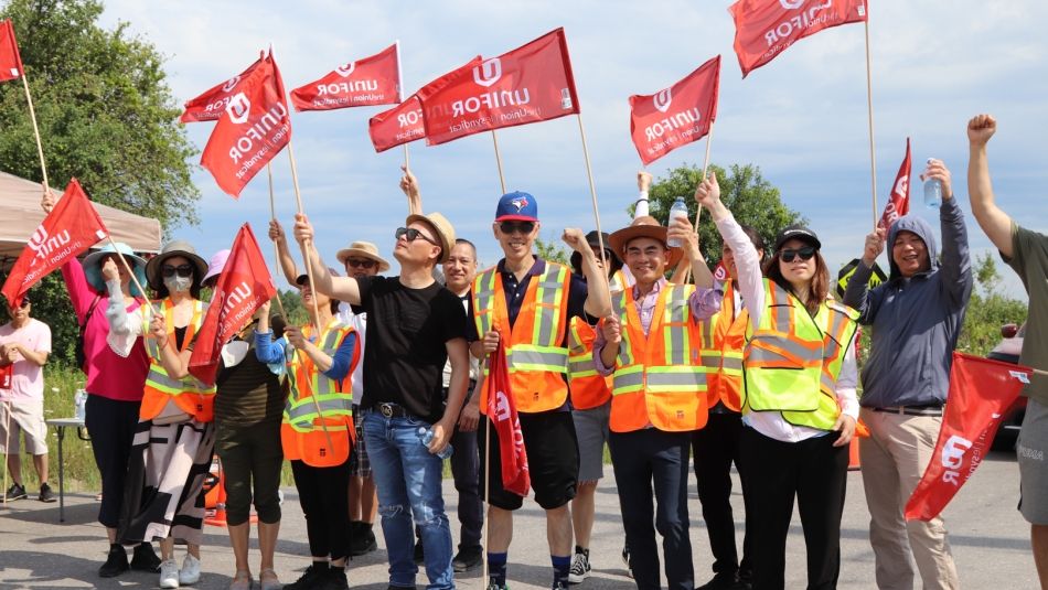Local 1090 members on the Pickering Casino Resort picket line. A line of Unifor members outdoors wearing high visibility vests and waving Unifor flags.