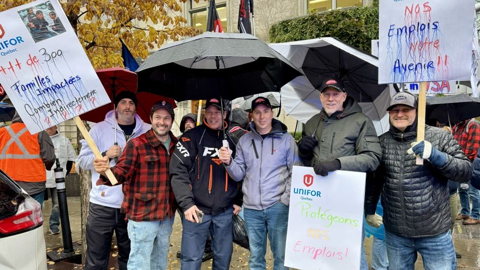 Un groupe d'hommes sous la pluie, tenant un grand parapluie, des pancartes et des drapeaux.