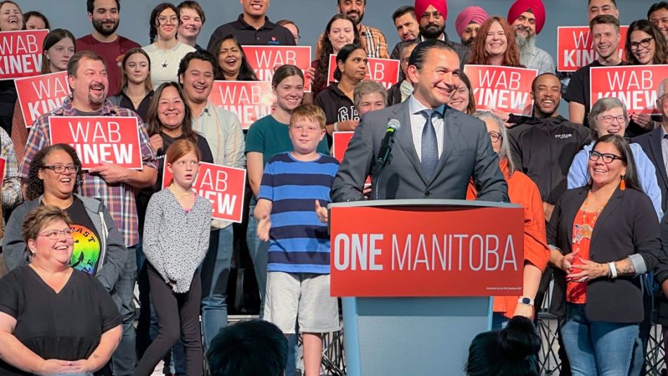 Man in suit at a podium with supporters behind him.