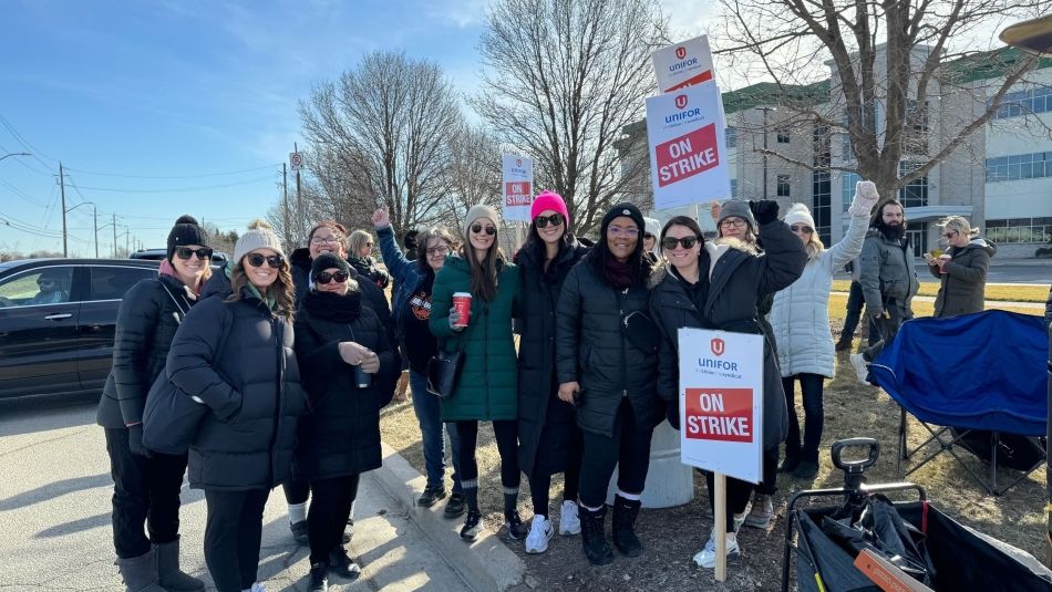 A large group of mostly women in warm winter cloths on a picket line holding up place cards.