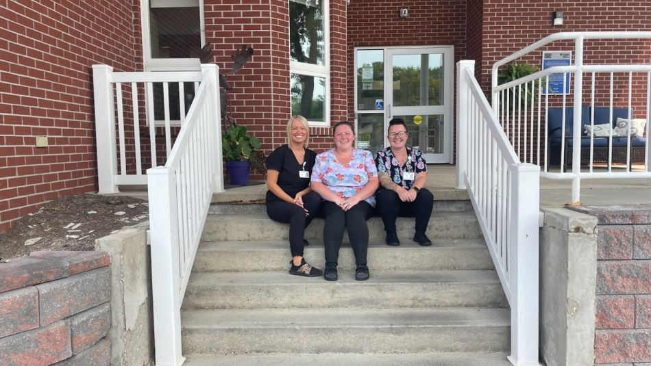 Three women sitting on the front entrance staircase smiling