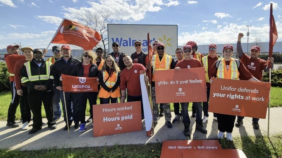Large group of workers posing with red pro-union signs. Walmart signage is visible behind them.
