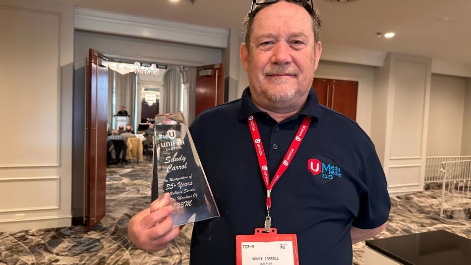 A man wearing a blue shirt holds up a glass award.