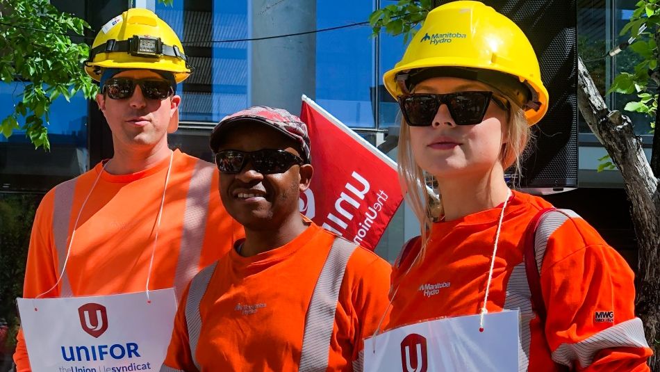 Three hydro workers, two with yellow hard hats, posing for a photo outside