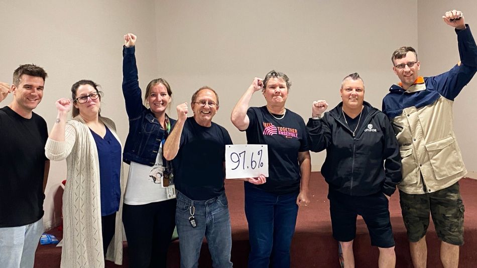 Local 2215 bargaining committee celebrates strike mandate Group of seven workers with fists held high hold sign saying 97.6%