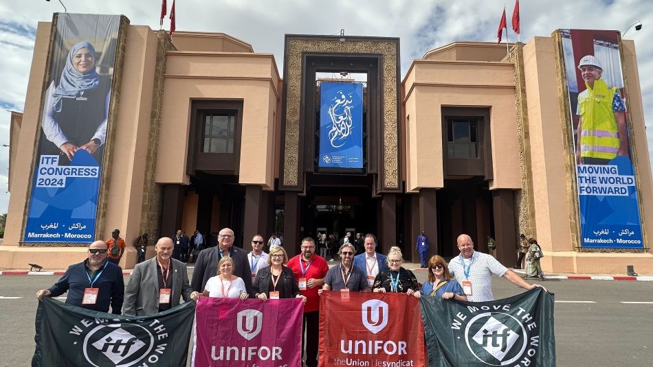 A large group standing outside hold up large Unifor and ITF flags