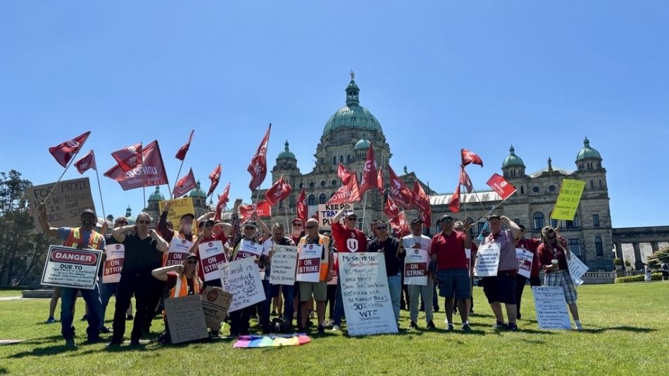 Gavin McGarrigle speaking from a glass podium with Shaun Bhoondpaul standing behind him. The BC legislature building with a giant Canadian flag is in the background.