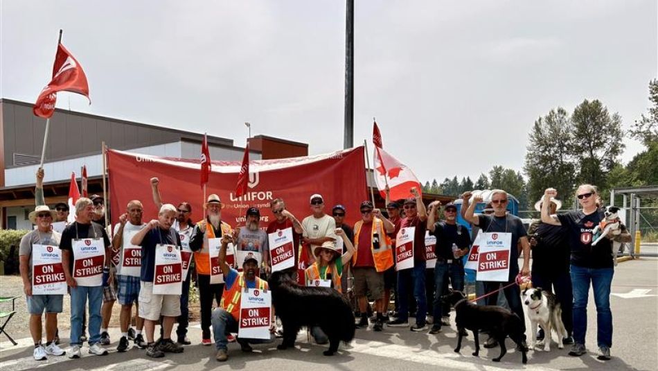 A large crowd holding up red Unifor flags and on strike placcards