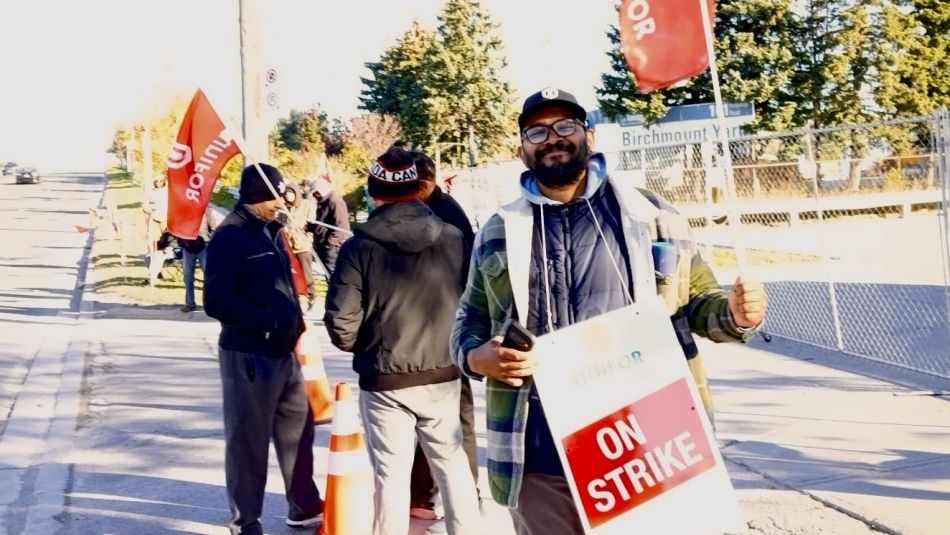 A man holding a "ON Strike" placcard and a red Unifor flag