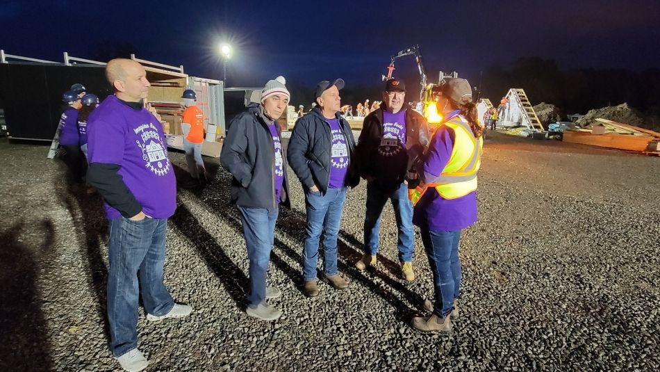 A group of people wearing purple shirts with a construction site in the background.