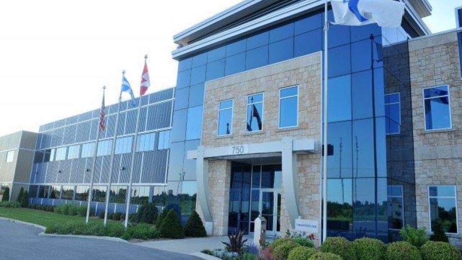 Building with glass and brick and four flags out front, with manicured hedges.