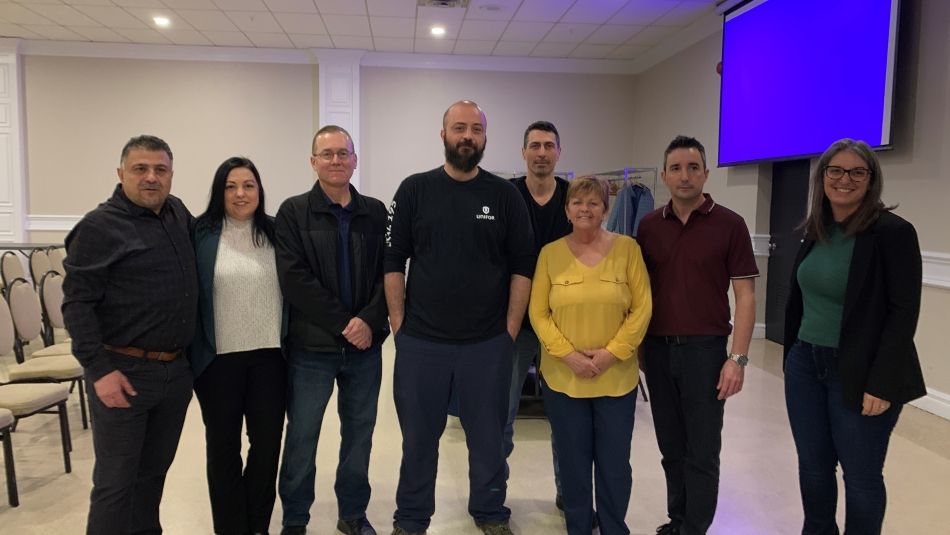 A group of people staning together with a blue screen in the right background.