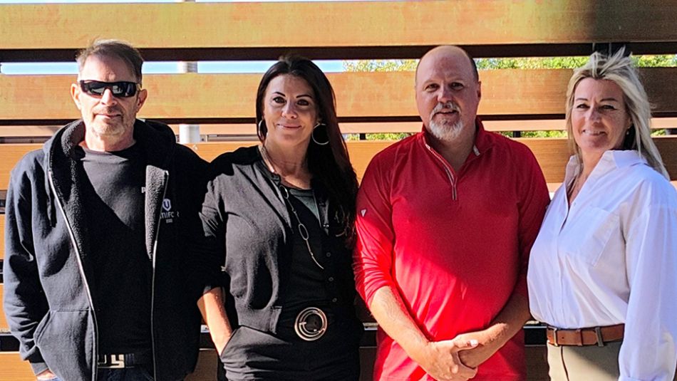 Four people pose outside in front of a wood fence 