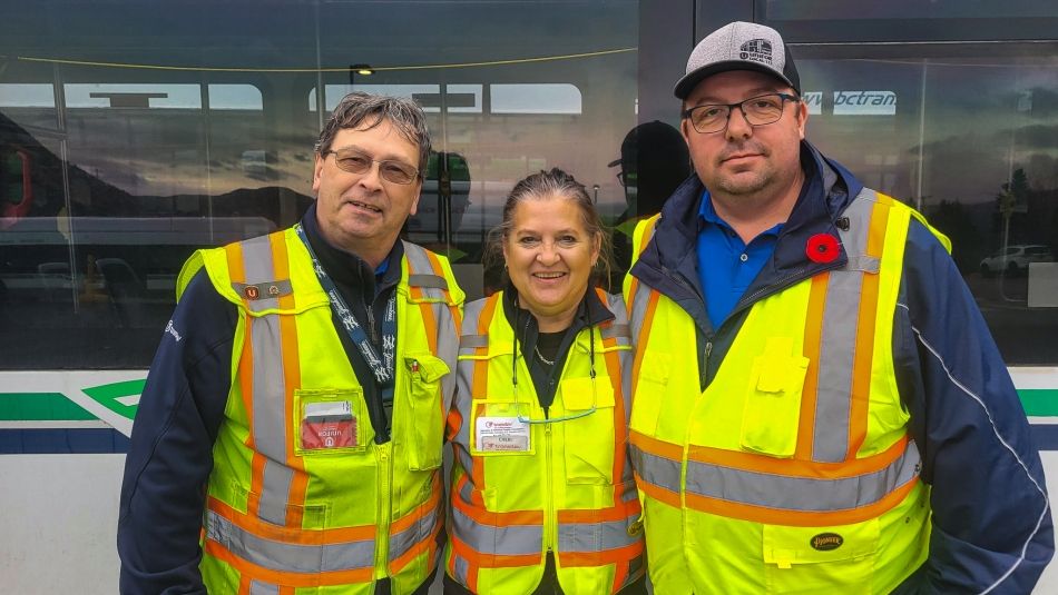 Three people in yellow safety vests in front of a bus.